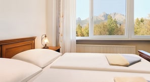 Ein Hotelzimmer mit zwei Betten, einem Nachttisch mit Lampe, einem Fenster mit Blick auf Berge und einer Heizung.