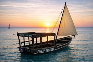 A traditional wooden boat named "Anaya Zanzibar" on calm waters during sunset.