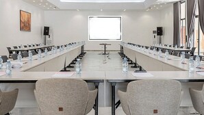 Une salle de conférence avec une longue table, des chaises, des bouteilles d’eau et un écran de projection.