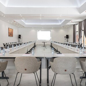 A conference room with a long table, chairs, water bottles, and a projector screen.