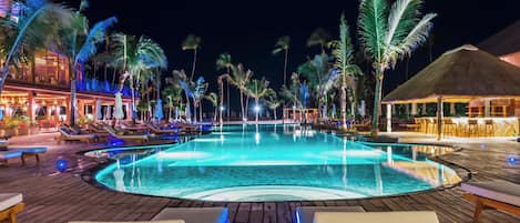 Área de piscina nocturna con sillones de descanso y una fuente.