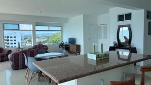 Cocina moderna con una isla grande, comedor con sillas y vistas a la ciudad.