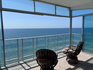 Un balcon avec vue sur l’océan, deux fauteuils en osier et un sol carrelé.