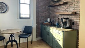 Una cocina con pared de ladrillo, ventana, fregadero y cafetera.