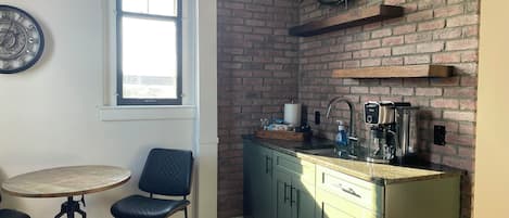 Et køkken med en murstensvæg, et vindue, en vask og en kaffemaskine.