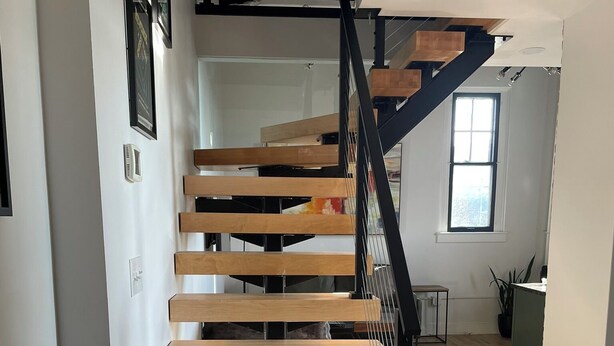 Una escalera moderna con escalones de madera y barandilla de metal negro, que lleva a un piso superior.