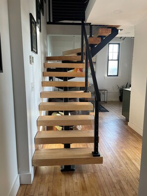 Una escalera moderna con escalones de madera y barandilla de metal negro, que lleva a un piso superior.