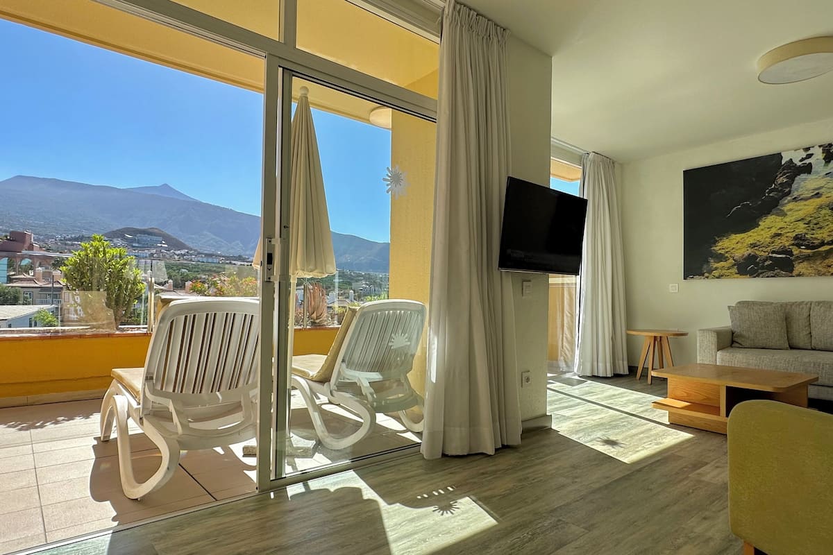A modern living room with a large window, a flat-screen TV, a sofa, and a dining table.