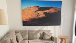 A living room with a sectional sofa, a coffee table, a rug, and a painting of a desert landscape.