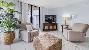 A living room with a sofa, armchair, ottoman, TV stand, and a large potted plant. - 🌴Gulf Views + Resort Amenities | Walk 2 Beach | Seaside Beach & Racquet 5914 (Orange Beach)