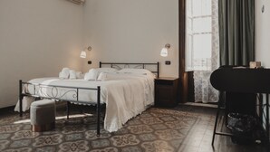 Een slaapkamer met een bed, nachtkastjes, een stoel, een prullenbak en een raam met gordijnen.