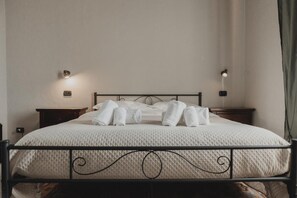 Un lit bien fait, avec des serviettes pliées, une tête de lit, des tables de chevet et des lampes fixées au mur.