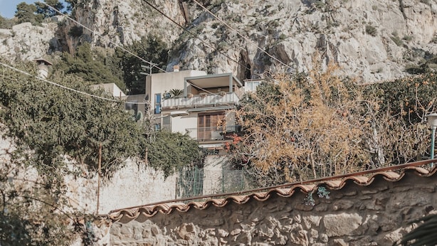 Un mur de pierre, un banc en bois et un bâtiment doté de balcons.