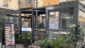 Un café en plein air avec un tableau affichant le menu, des plantes en pot et une terrasse dallée de pierres.
