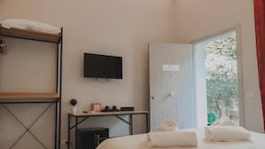 Une chambre d’hôtel avec un lit, une télévision, un bureau agrémenté d’une plante et une fenêtre donnant sur des arbres.