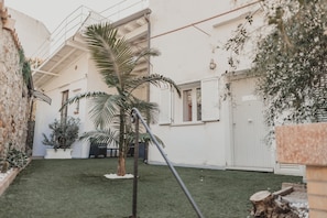 Une cour avec un palmier, un bâtiment blanc doté d’un balcon et une porte en bois.