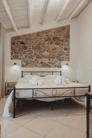 Ein Schlafzimmer mit Steinwand, einem Bett mit weißer Bettwäsche, zwei Nachttischen und einer Decke mit freiliegenden Balken.