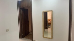 A hallway with a wooden door leading to another room, a mirror on the wall, and a light switch. - Burj Malaak apartment in a private residence with swimming pool (Marrakech)