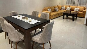 A modern living room with a dining table and chairs, a sofa with patterned cushions, and a coffee table. - Burj Malaak apartment in a private residence with swimming pool (Marrakech)