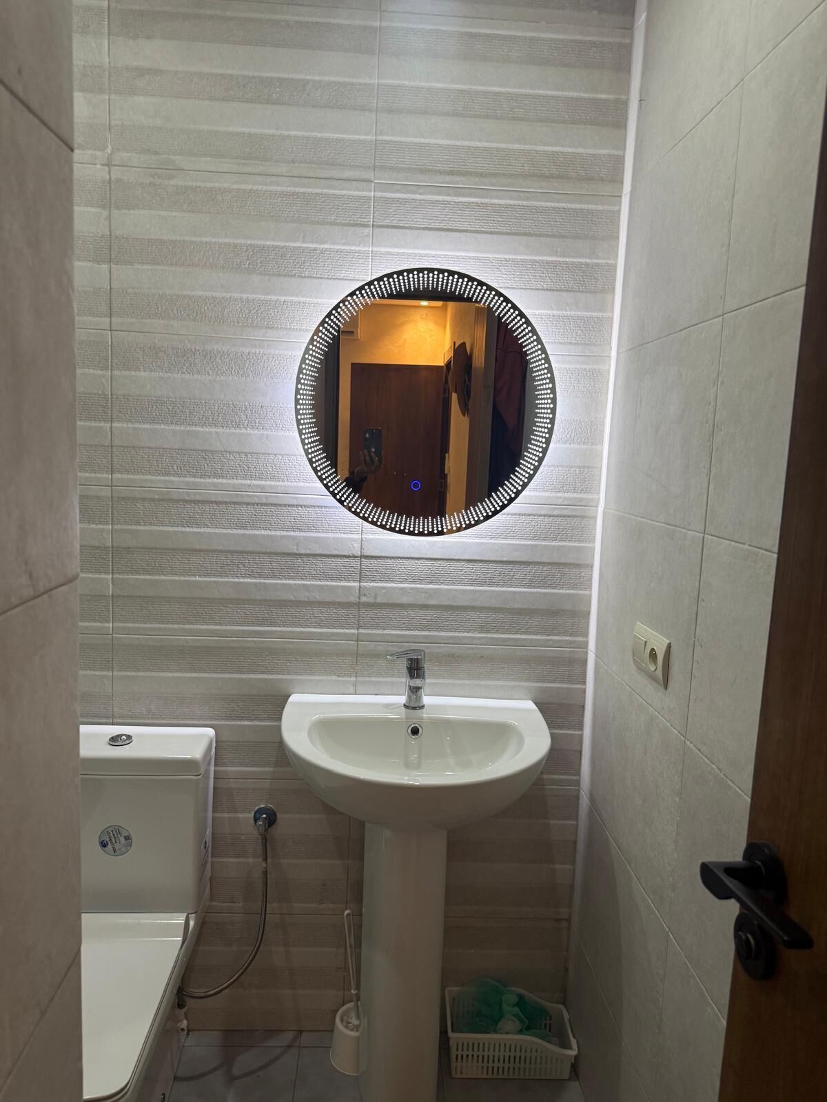 Um banheiro com pia branca, espelho com moldura iluminada e vaso sanitário.