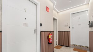 Un couloir avec des portes, un extincteur et un paillasson.