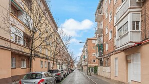 Une rue résidentielle bordée de voitures garées, avec des immeubles à plusieurs étages et des arbres sans feuilles.