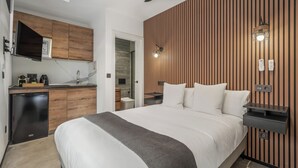 Une chambre d’hôtel moderne équipée d’un lit, d’un bureau, d’une cuisine intégrée et d’un ventilateur de plafond.