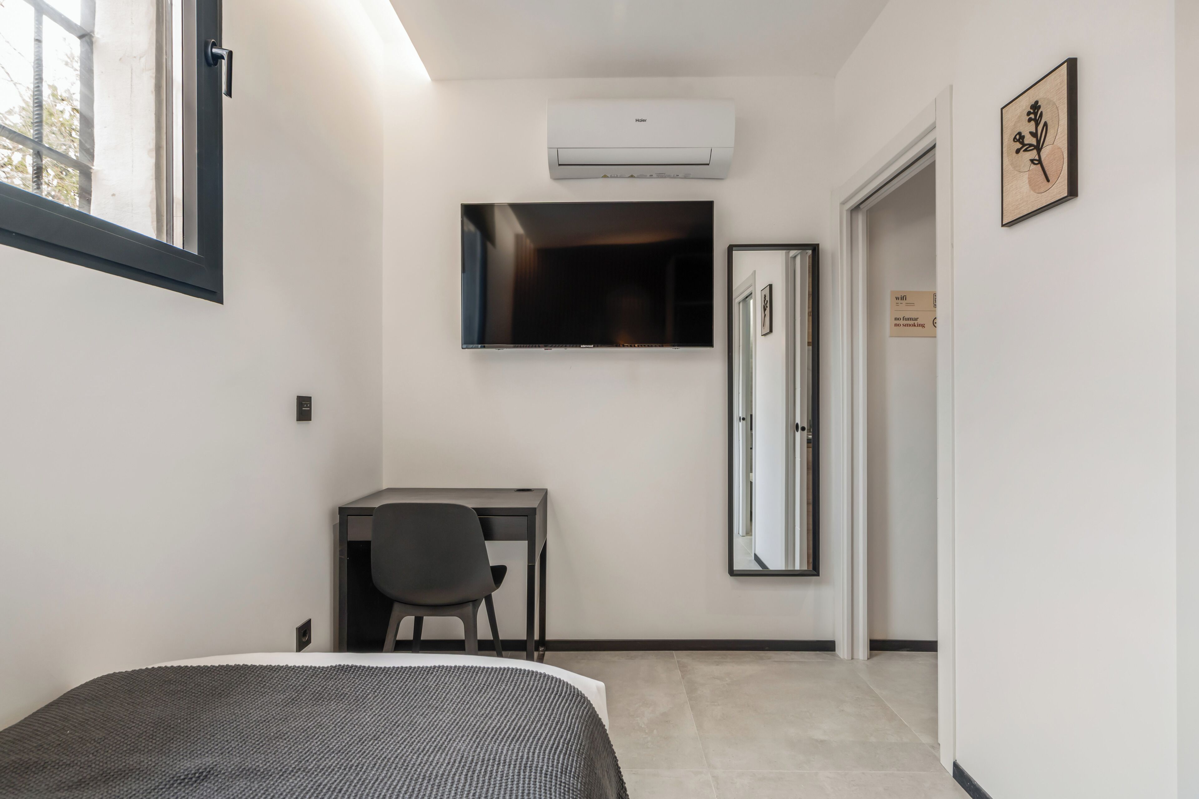 Une chambre d’hôtel comprenant un lit, un bureau, une chaise, une télévision, un appareil de climatisation et une porte.