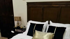 Un lit bien fait, avec du linge de lit blanc, un coussin doré et deux serviettes disposées en forme de cœur.