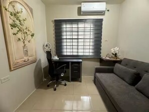 A room with a desk, a chair, a sofa, a window with blinds, a wall-mounted air conditioner, and a decorative plant. - Very Safe Clean Comfortable, Excellent Location
Renovated Townhouse San Fernando (San Fernando)