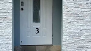 Une porte blanche portant le numéro 3, encastrée dans un mur à la texture de pierre.