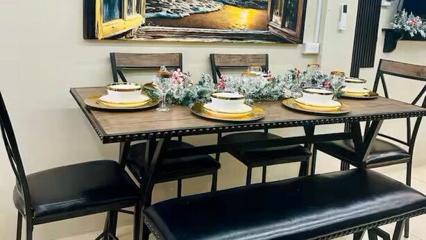 Un coin repas avec une table dressée pour quatre personnes, agrémenté d’un tableau représentant un coucher de soleil sur l’océan.