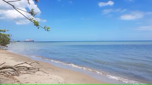 Une plage à l’eau claire, un navire à l’horizon et un ciel dégagé.