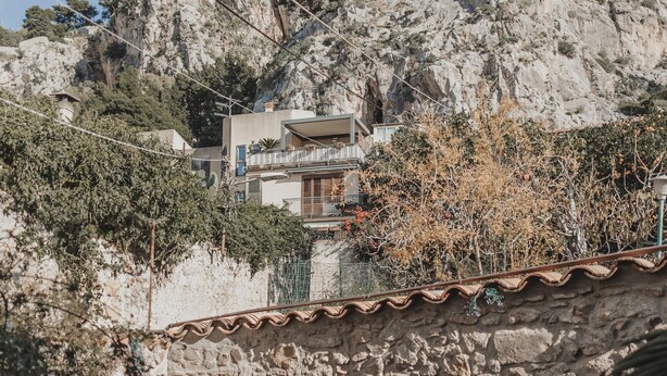 Un muro in pietra con ringhiera metallica, una panca di pietra e un piccolo giardino.