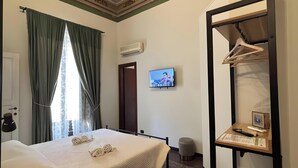 Una camera d'albergo con un letto, una TV, un armadio e un tavolino con sopra degli oggetti.
