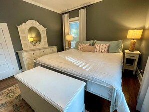 A bedroom with a large bed, a dresser, a mirror, two bedside tables with lamps, and a window with curtains. - Good Ol' Country Farmhouse (Moncure)