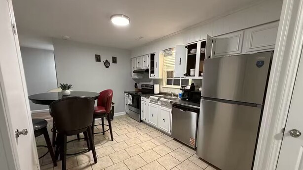 Una cucina funzionale con mobili bianchi, un frigorifero in acciaio inossidabile, un tavolo con sedie e una piccola pianta in vaso.