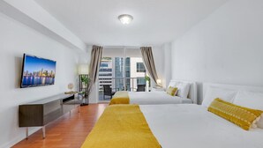 Ett modernt hotellrum med en stor säng, ett skrivbord, en tv och en balkong med gardiner.
