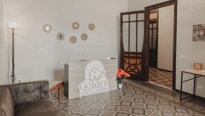 Un comptoir d’accueil avec une enseigne « Golden House », un sol à motifs, un canapé, une lampe et une porte donnant sur une autre pièce.