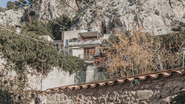 Un mur de pierre, un banc en bois et un bâtiment doté de balcons.