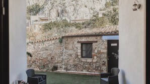 Un bâtiment en pierre avec une petite fenêtre, une porte et un toit recouvert de tuiles. On aperçoit deux chaises en osier et une petite table au premier plan.