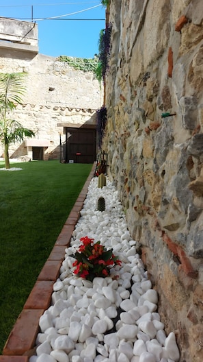 Un muro de piedra con un sendero de grava, un cactus y flores rojas.