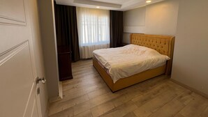 Une chambre à coucher avec un lit, un plancher en bois, une armoire et une fenêtre avec des rideaux.
