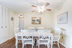 A dining area with a white table and chairs, a ceiling fan, and a framed picture on the wall. - Braemar Towers S 1406 (Ocean City)