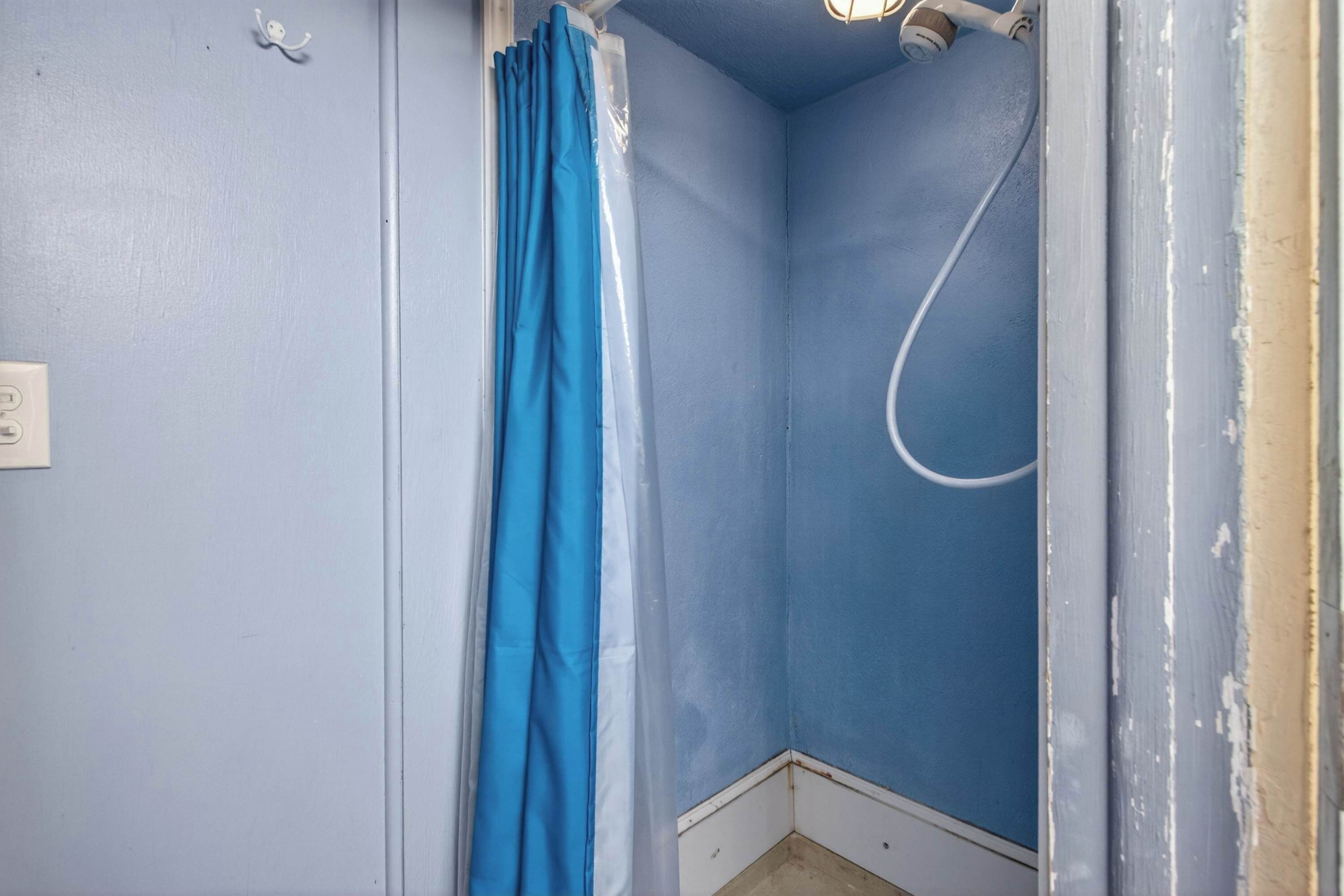 Une salle de bain avec des murs bleus, un rideau de douche et un tuyau de douche visible.