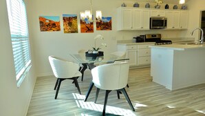 A modern kitchen with white cabinetry, a central island, and a dining area with two chairs. - Beautiful 3/2 Designer Home with Golf Cart & Dog Friendly – Village of Dabney (The Villages)