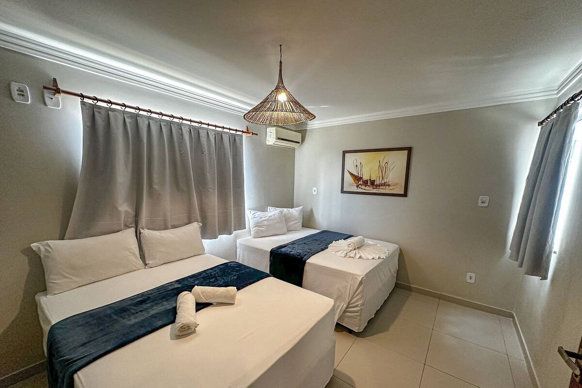 A hotel room with two beds, a painting on the wall, a ceiling light fixture, and a window with curtains.