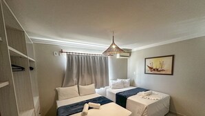 A hotel room with two beds, a ceiling fan, a painting on the wall, and a window with curtains. - Enseada Mutá (Porto Seguro)
