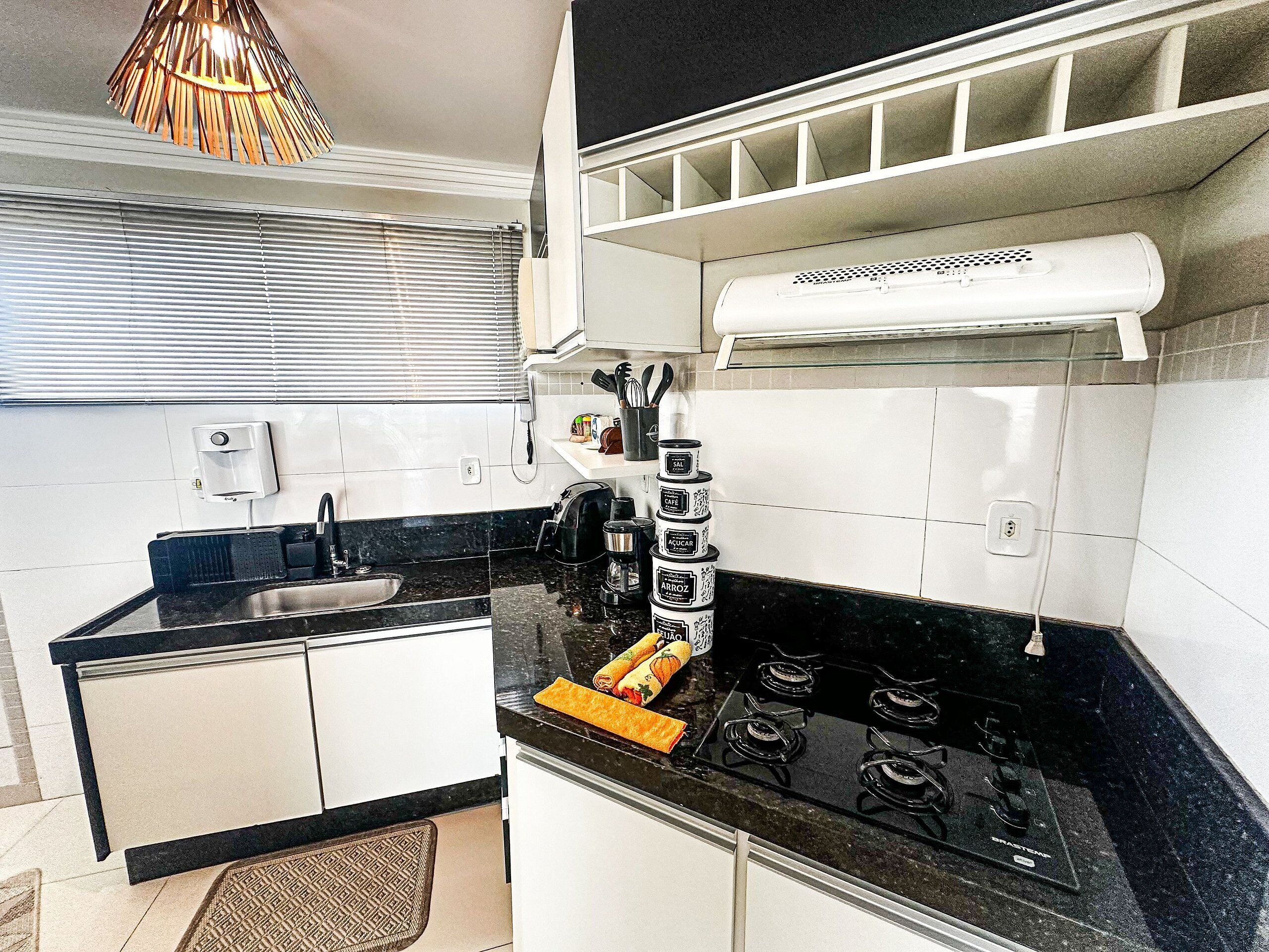 A kitchen with a gas stove, a coffee maker, and a hanging pot rack.