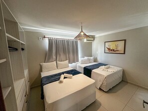 A hotel room with two beds, a ceiling fan, a painting on the wall, and a window with curtains. - Enseada Mutá (Porto Seguro)